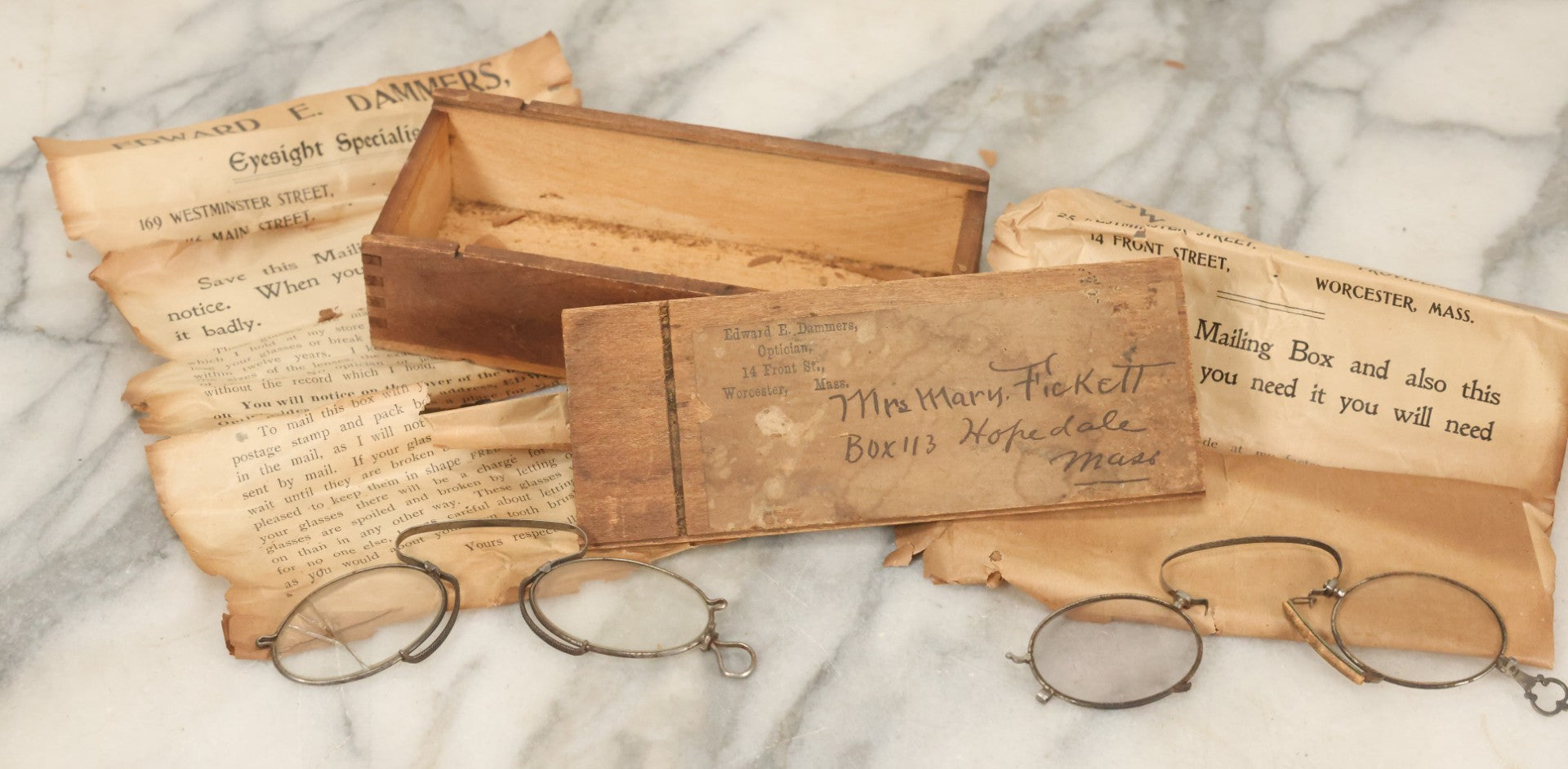 Lot 079 - Antique Slide Top Wooden Mailing Box From Edward E Dammers, Optician, Worcester, Massachusetts, Containing Two Pairs Of Antique Eyeglasses And Advertising Ephemera, Addressed To Mary Fickett, As Found, Note Cracks And Wear