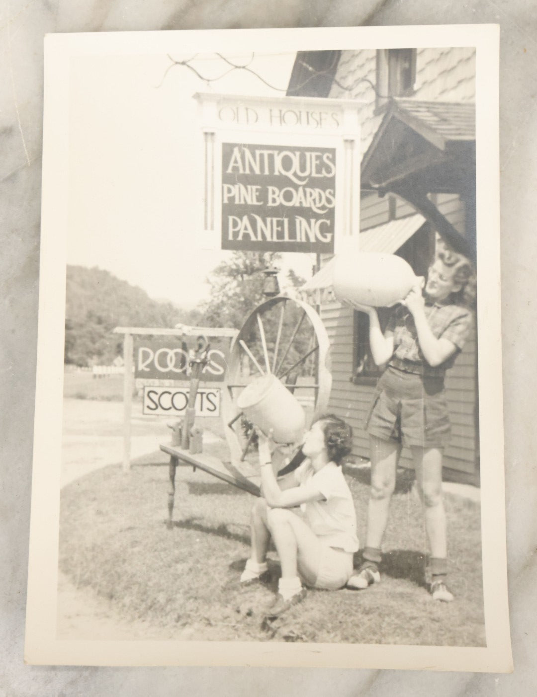 Lot 126 - Vintage 5 x 7 Snapshot Photograph Of Two Young Women Outside An Antique Store Pretending To Drink Whiskey From Old Jugs