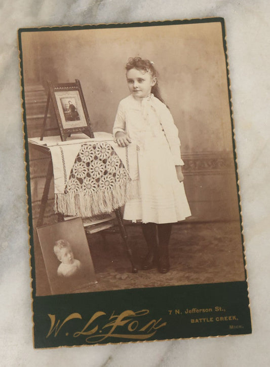 Lot 130 - Antique Cabinet Card Photograph Of Young Girl In White Dress Posing Next To Table With Photos In Picture, P.I.P., W.L. Fox Photographer, Battle Creek, Michigan, Identified As Anna May Downs