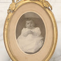 Lot 064 - Antique Oval Boarded Photograph Of Young Baby In White Gown In Brass Frame With Iris Flower Motif, 4-3/8" x 6-1/2"