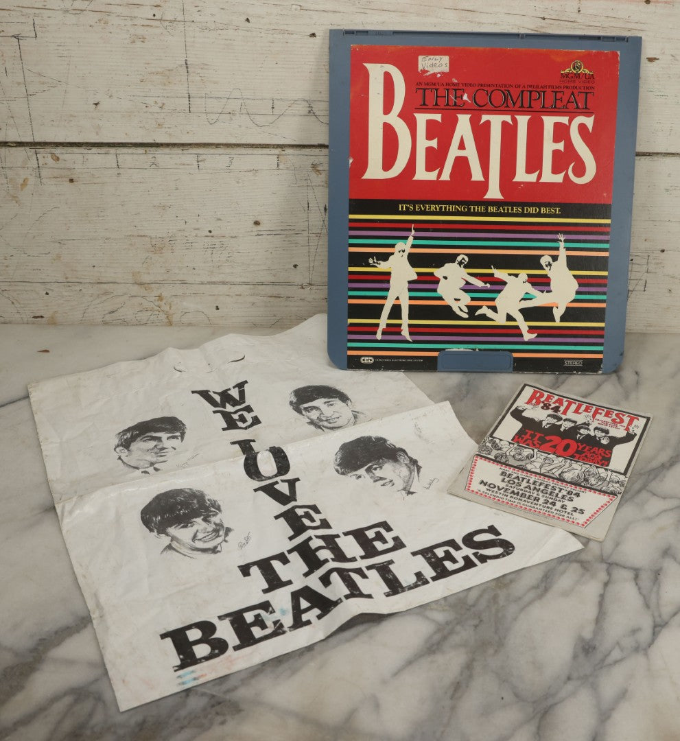 Lot 041 - Vintage "The Beatles" Band Collectibles Three Piece Grouping Including Plastic "We Love The Beatles" Shopping Bag, "The Compleat Beatles" Laserdisc, And Beatlefest 1984 Program