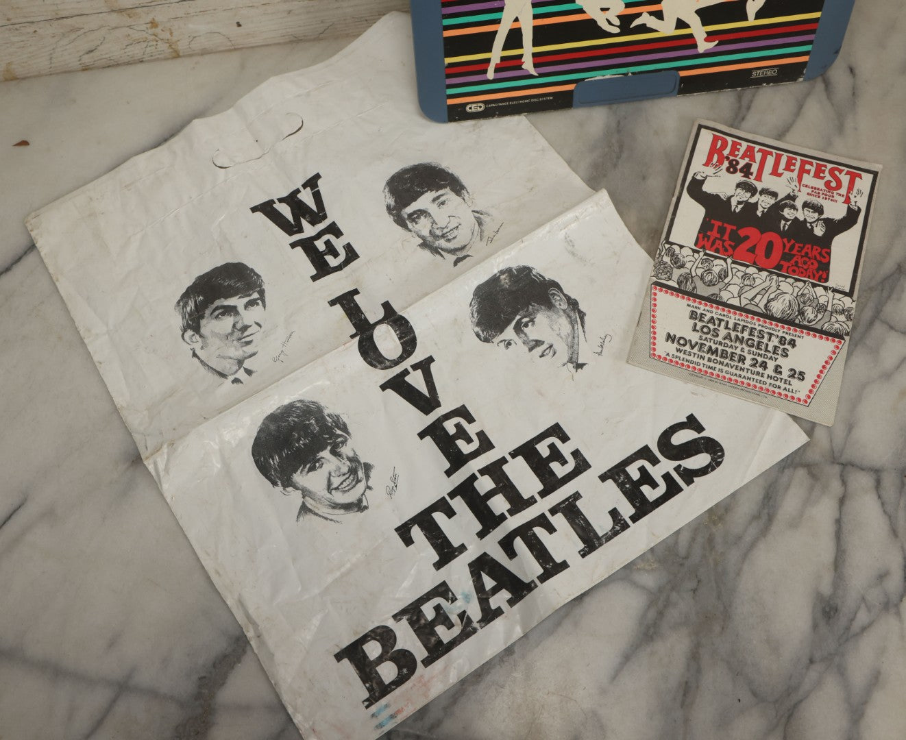Lot 041 - Vintage "The Beatles" Band Collectibles Three Piece Grouping Including Plastic "We Love The Beatles" Shopping Bag, "The Compleat Beatles" Laserdisc, And Beatlefest 1984 Program