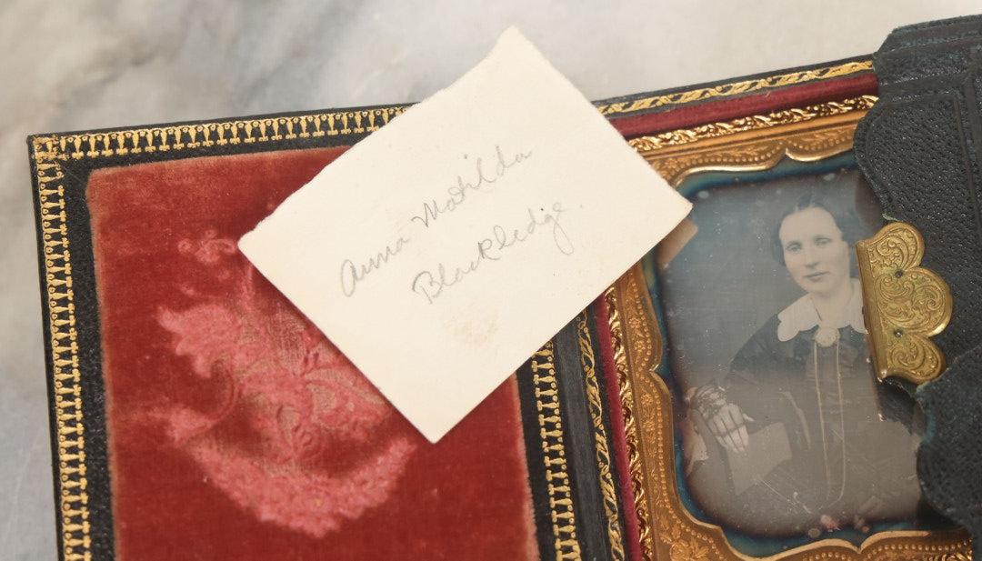 Lot 115 - Antique 1/6th Plate Daguerreotype Photograph Of Young Woman Wearing Black Lace Gloves And Large Brooch In Leatherette Folder Case With Latch, "Bijou" Lettering On Spine, Identified As Anna Matilda Blackledge, Note Partial Tear On Case Cover