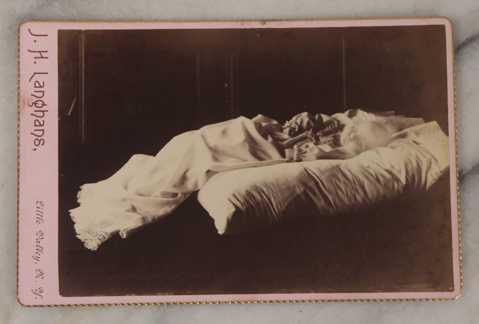 Lot 027 - Antique Cabinet Card Postmortem Photograph Of Baby Laying On Pillows With Dark Background, J.H. Langhans, Photographer, Little Valley, New York