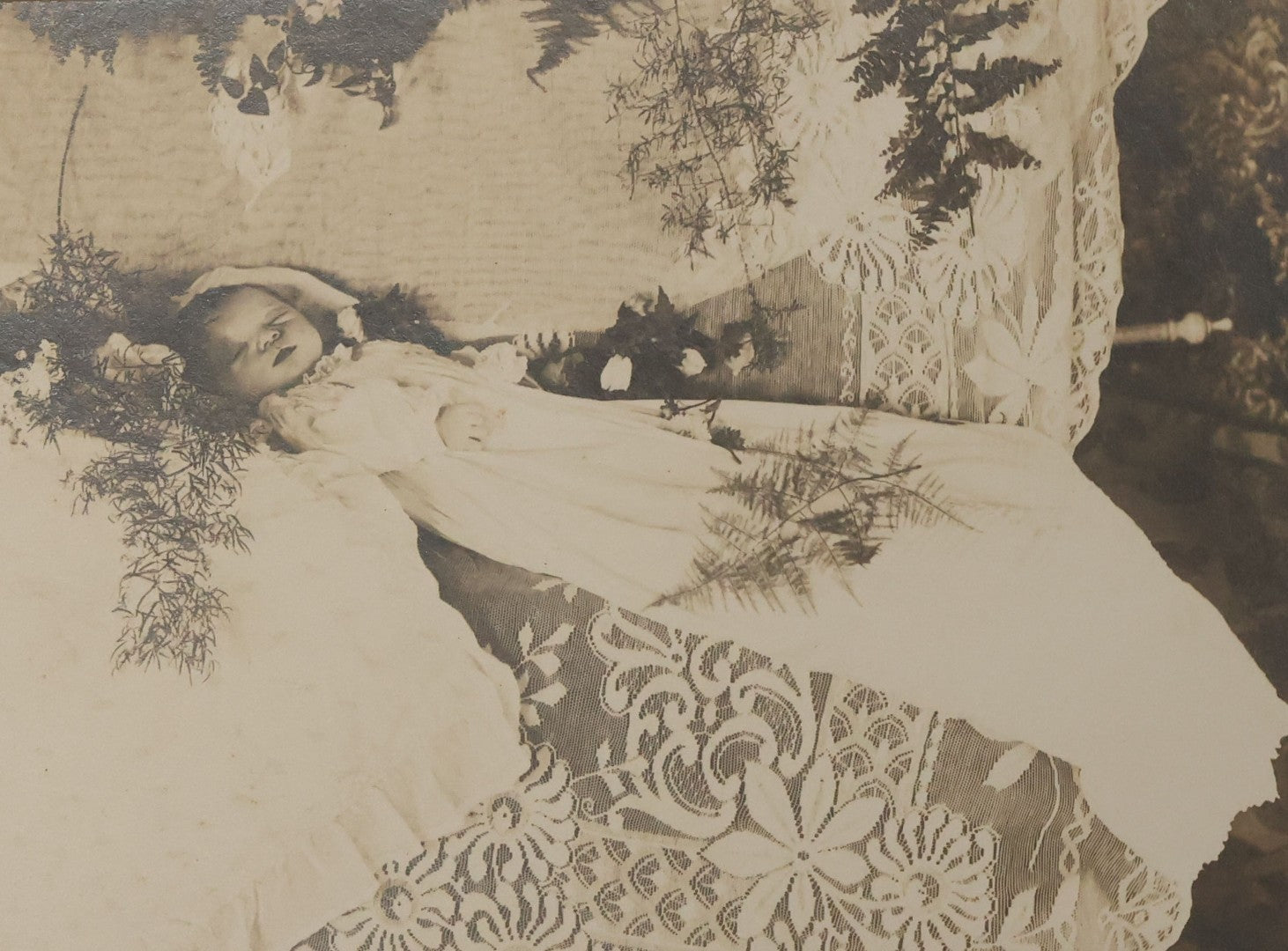 Lot 030 - Antique Boarded Post Mortem Photograph Of Baby In Long White Robes, Laid Out On Lace Floral Linens With Flowers