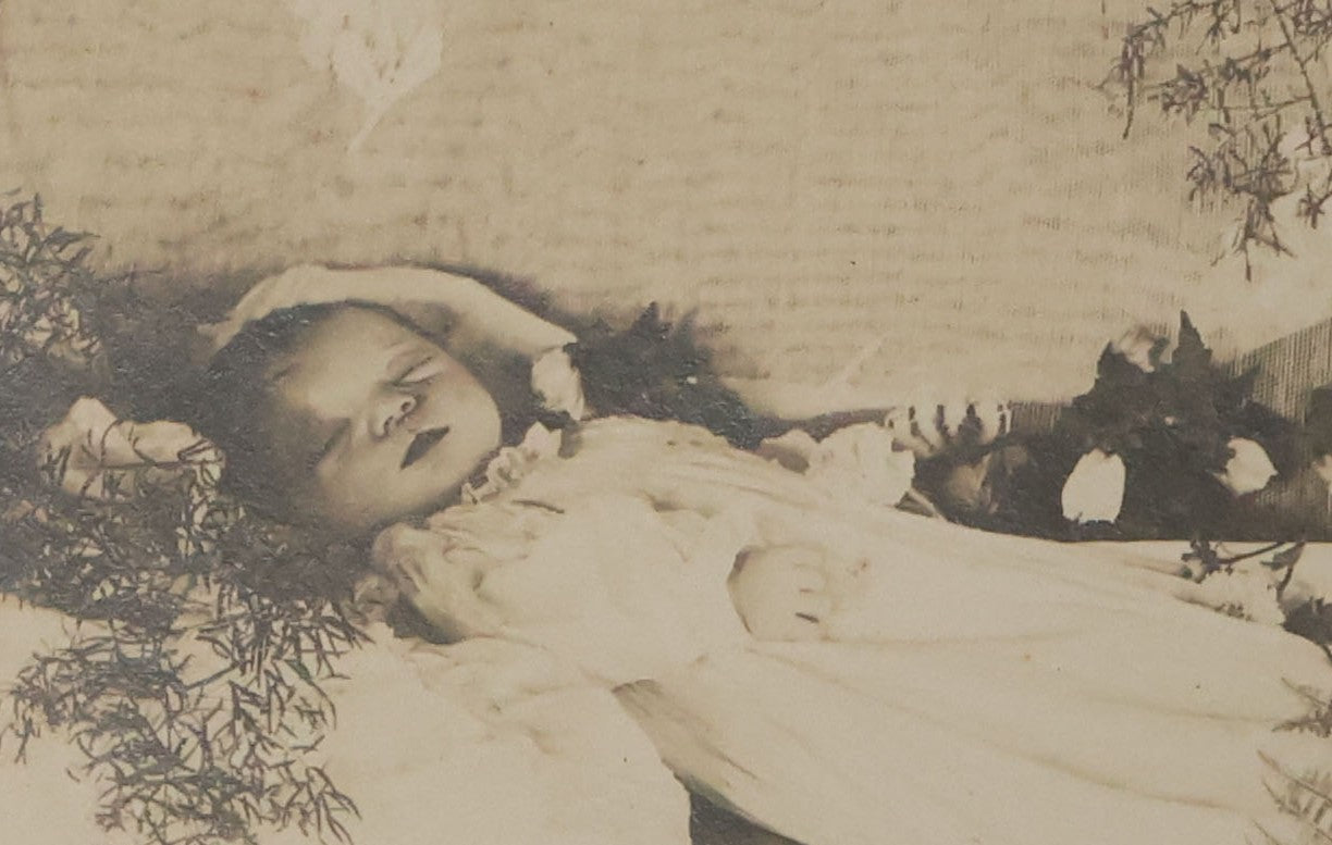 Lot 030 - Antique Boarded Post Mortem Photograph Of Baby In Long White Robes, Laid Out On Lace Floral Linens With Flowers