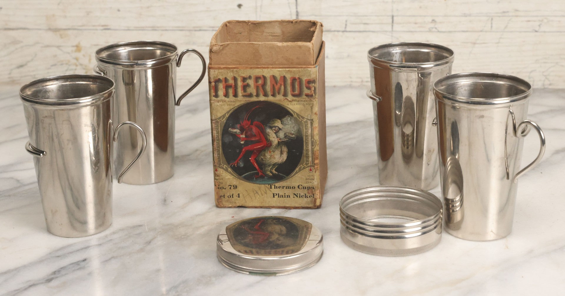 Lot 048 - Antique Thermos Brand Thermo Cup Set Of Four Plain Nickel Cups No. 79, With Original Box With Devil Graphics, Manufactured By The American Thermos Bottle Co., New York, Patented 1912, Complete Set