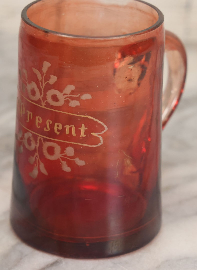 Lot 066 - Antique Ruby Glass Mug With Hand Etched, Hand Painted Details, "A Present" With Flowers, Note Chip To Bottom Of Handle, Rim