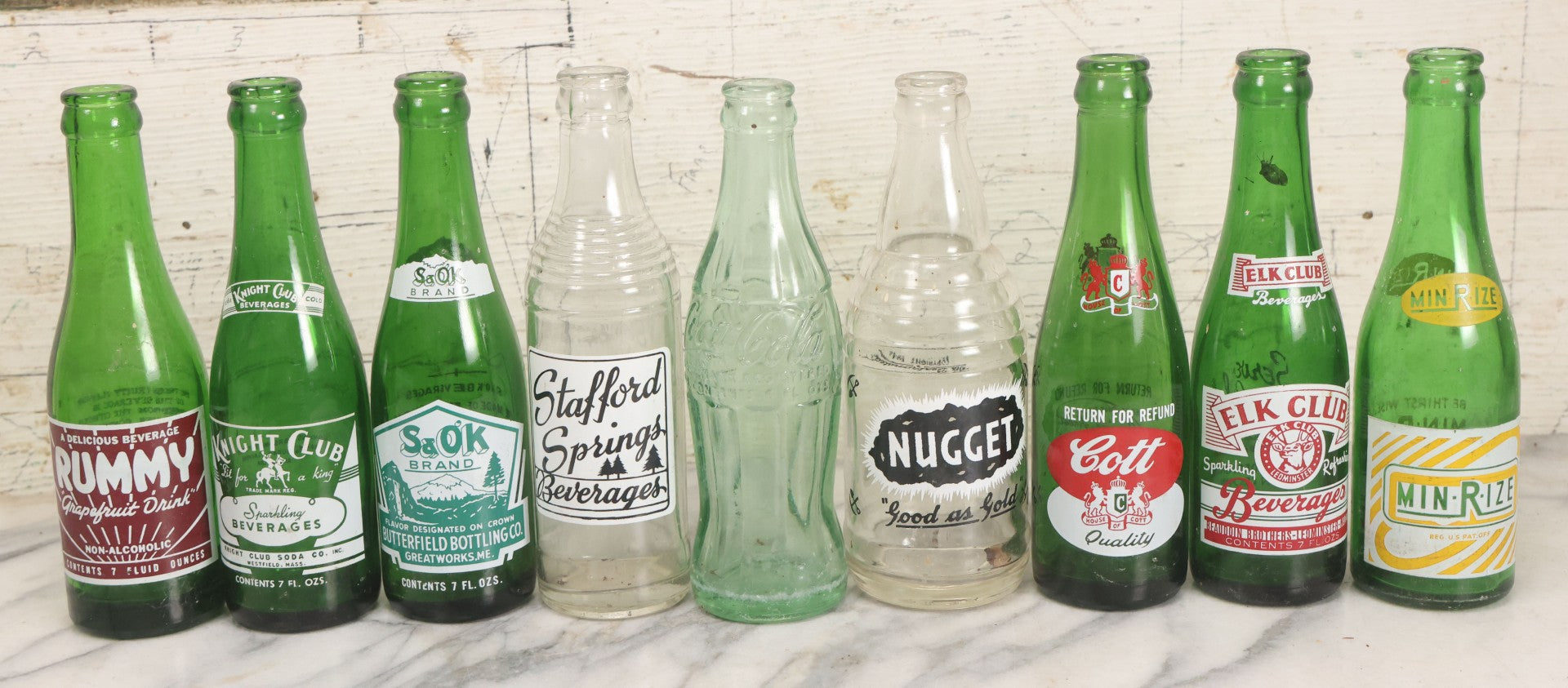 Lot 057 - Grouping Of Nine Vintage Glass Soda Bottles Including Coca-Cola, Cott, Min-R-Ize, Elk Club, Knight Club, Nugget, S&O'K, Rummy Grapefruit Drink, And Stafford Springs