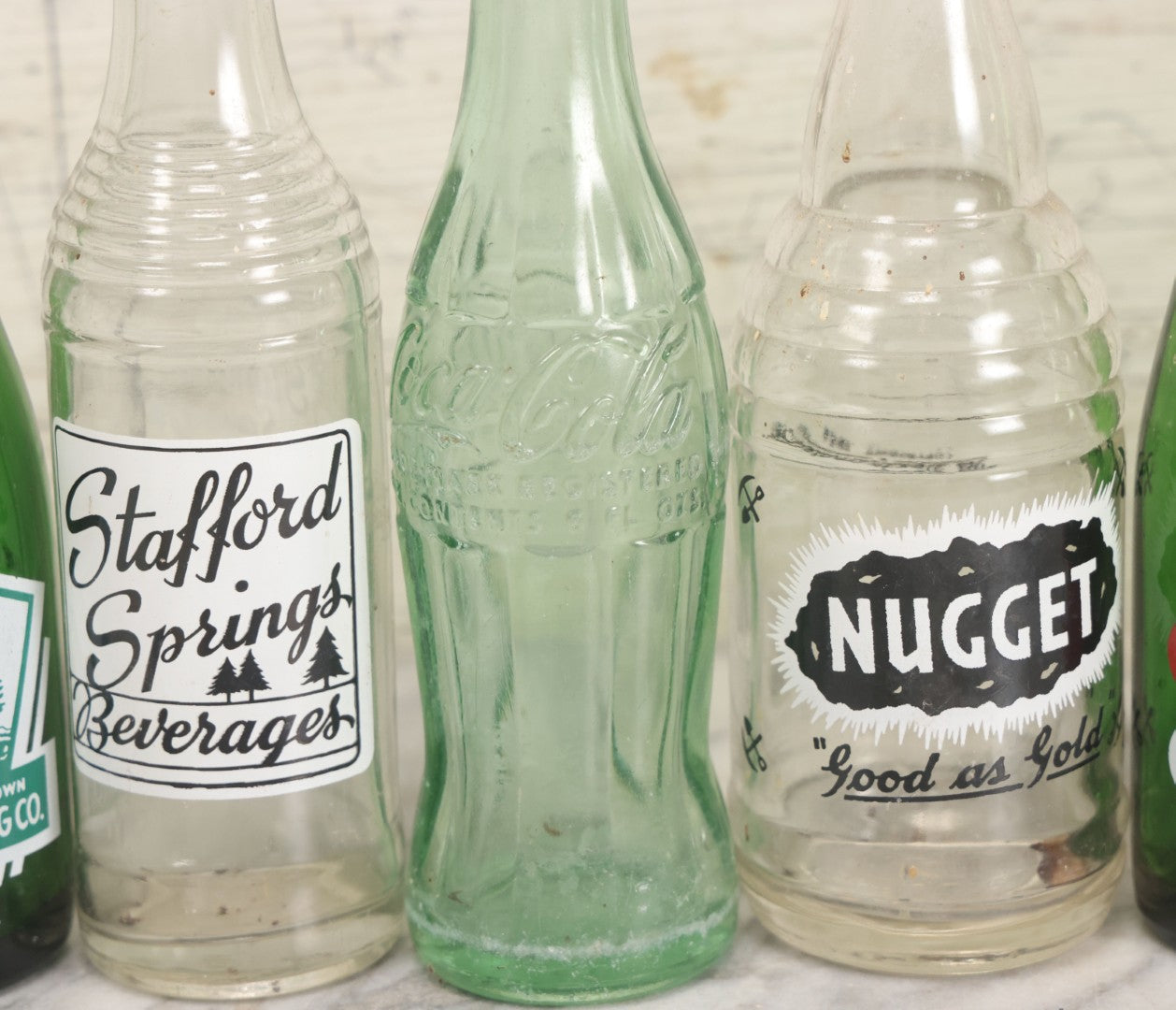 Lot 057 - Grouping Of Nine Vintage Glass Soda Bottles Including Coca-Cola, Cott, Min-R-Ize, Elk Club, Knight Club, Nugget, S&O'K, Rummy Grapefruit Drink, And Stafford Springs