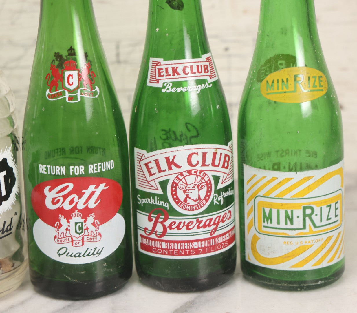 Lot 057 - Grouping Of Nine Vintage Glass Soda Bottles Including Coca-Cola, Cott, Min-R-Ize, Elk Club, Knight Club, Nugget, S&O'K, Rummy Grapefruit Drink, And Stafford Springs