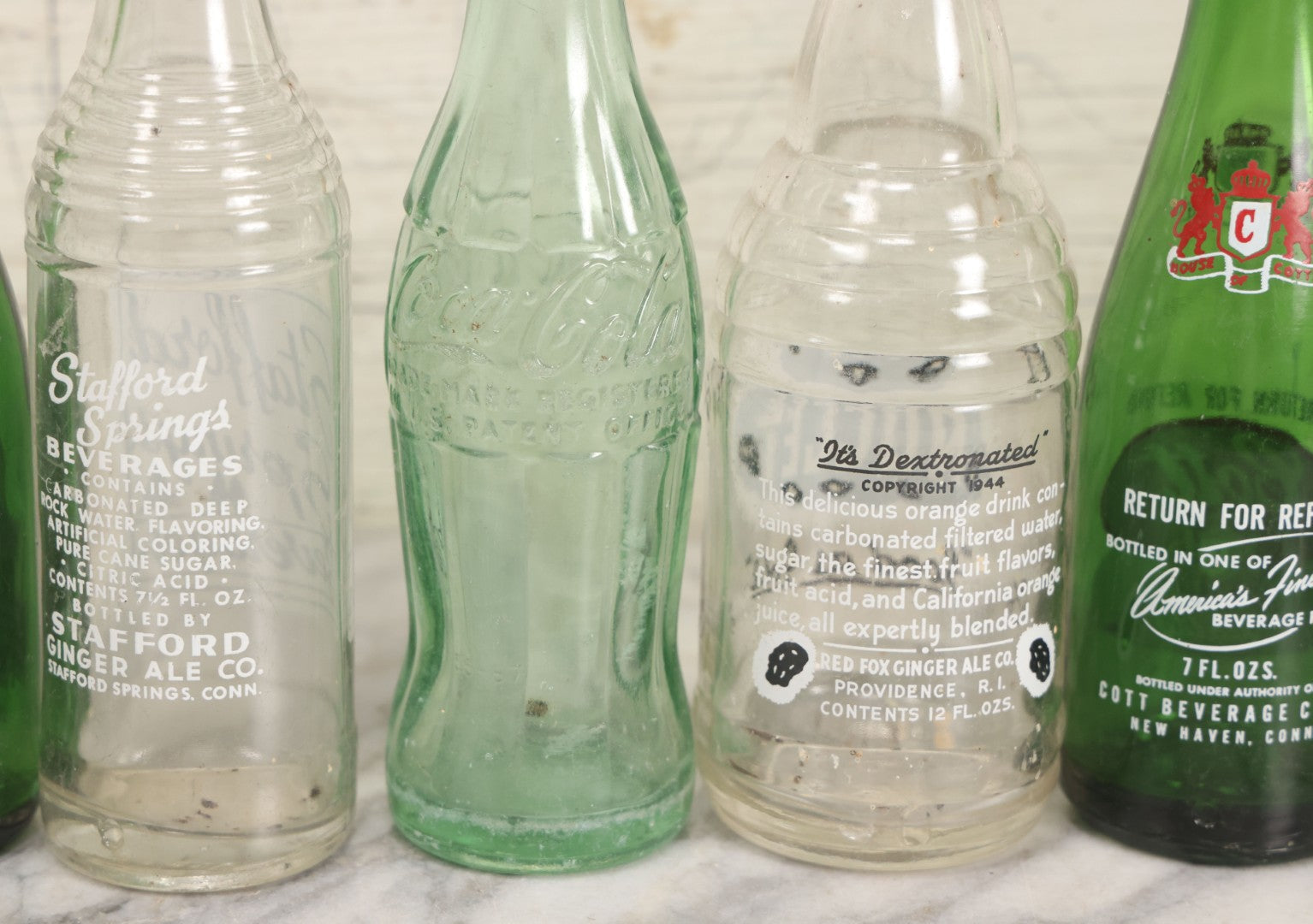 Lot 057 - Grouping Of Nine Vintage Glass Soda Bottles Including Coca-Cola, Cott, Min-R-Ize, Elk Club, Knight Club, Nugget, S&O'K, Rummy Grapefruit Drink, And Stafford Springs