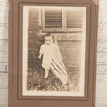 Lot 075 - Antique Boarded Photograph Of Toddler Standing Behind An American Flag In Front Of A Brick Wall With Shutters