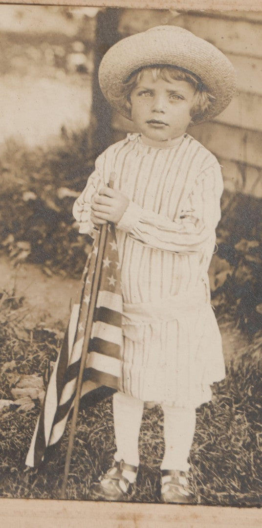 Lot 076 - Antique Boarded Photograph Of Young Child In Striped Shirt And Hat Standing With An American Flag In The Grass