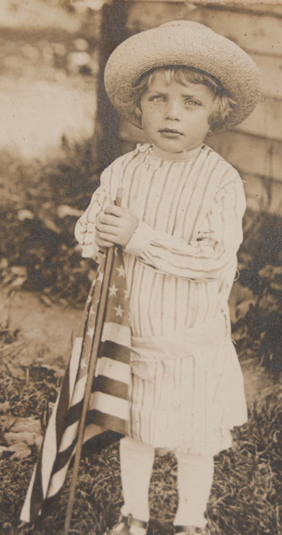 Lot 076 - Antique Boarded Photograph Of Young Child In Striped Shirt And Hat Standing With An American Flag In The Grass