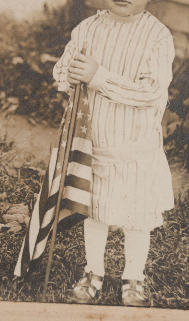 Lot 076 - Antique Boarded Photograph Of Young Child In Striped Shirt And Hat Standing With An American Flag In The Grass