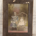Lot 077 - Antique Boarded Tinted Photograph Of Young Girl In Blue Dress Standing Besides Wicker Chair With Her Period China Doll, Note Color Tinting Notes On Verso