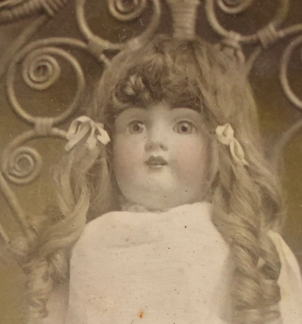 Lot 077 - Antique Boarded Tinted Photograph Of Young Girl In Blue Dress Standing Besides Wicker Chair With Her Period China Doll, Note Color Tinting Notes On Verso