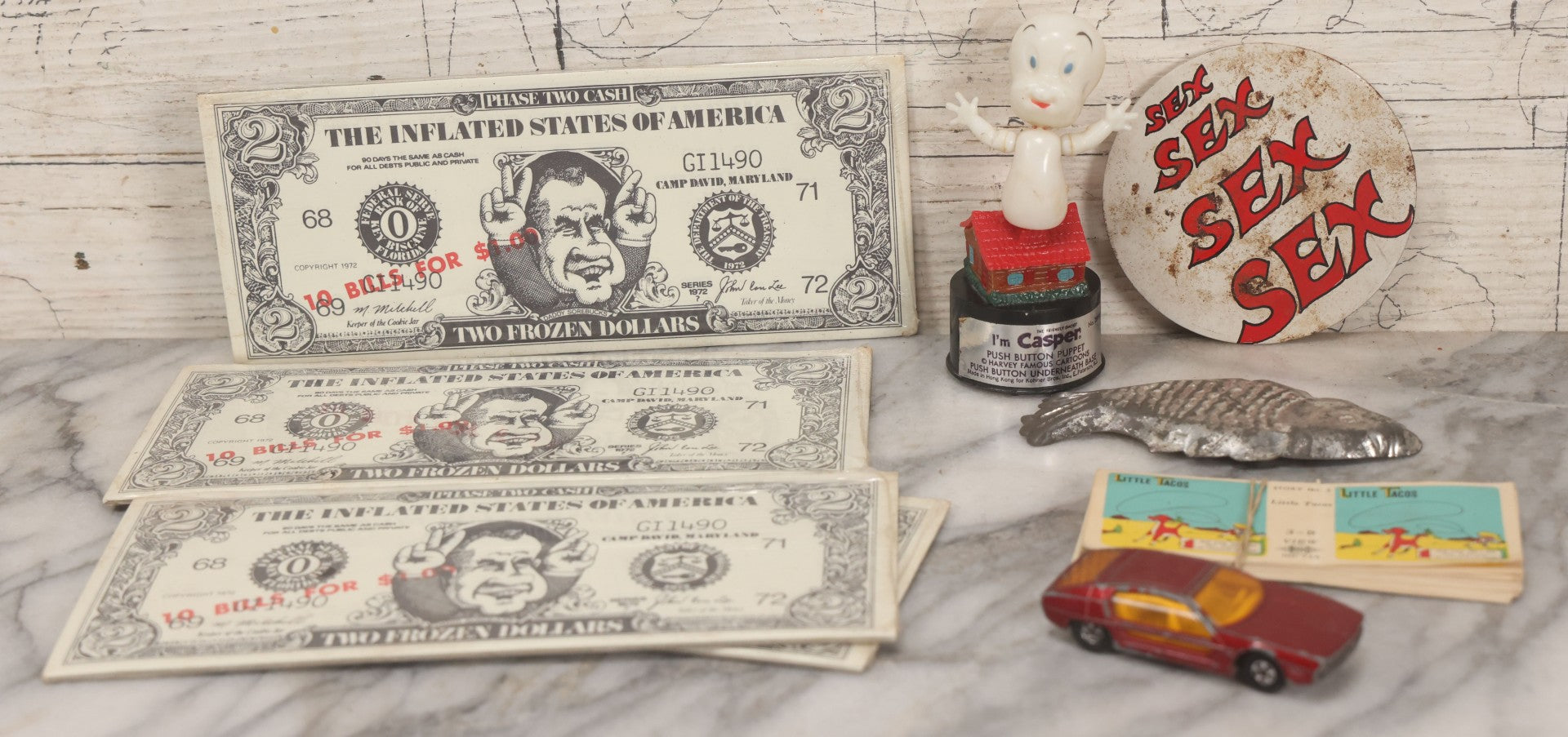 Lot 090 - Miscellaneous Novelties Grouping Including Casper The Friendly Ghost Push Button Puppet, Rusty Sex Pinback Button, Four "Inflated States Of America" Richard Nixon Dollars, Little Tacos 3D View Comic Book, Toy Sports Car, And Tin Fish