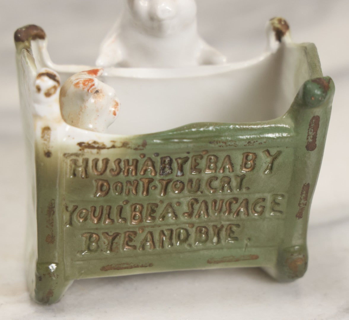 Lot 027 - Antique Porcelain Novelty Vessel With Mama Pig And Pig In Cradle, "Hush Hushabye Baby, Don't You Cry, You'll Be A Sausage Bye And Bye," Stamped Germany, With Remnants Of Original Paint, Note Cracks And Repairs