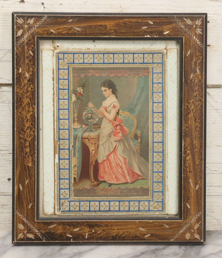 Lot 032 - Antique Lithographed Paper Board Box Cover Depicting Young Woman In Pink Dress Playing With Her Goldfish In Period Etched Wooden Frame, 10-5/8" x 11-3/4"