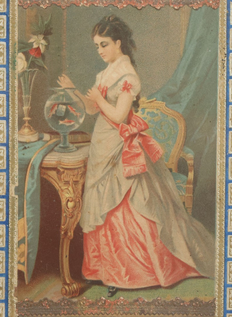 Lot 032 - Antique Lithographed Paper Board Box Cover Depicting Young Woman In Pink Dress Playing With Her Goldfish In Period Etched Wooden Frame, 10-5/8" x 11-3/4"