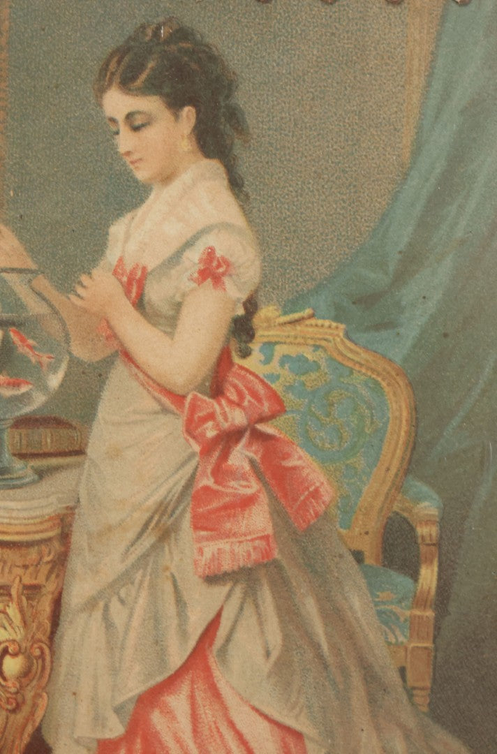 Lot 032 - Antique Lithographed Paper Board Box Cover Depicting Young Woman In Pink Dress Playing With Her Goldfish In Period Etched Wooden Frame, 10-5/8" x 11-3/4"