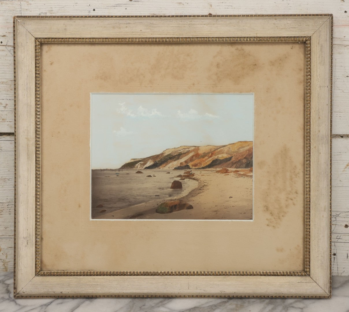 Lot 033 - Antique Painted Over Photograph Of Oceanside Cliffs And Beach With Child Seated On Rocks Likely Gay Head Cliffs, Martha's Vineyard, Massachusetts, In Original Frame, 17-1/2" x 15-1/2"