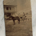 Lot 074 - Antique Outdoor Tintype Photograph Of Man In Stovepipe Hat Sitting On Horse Drawn Cart In Front Of A Building With Partial Sign Visible And Houses In Background