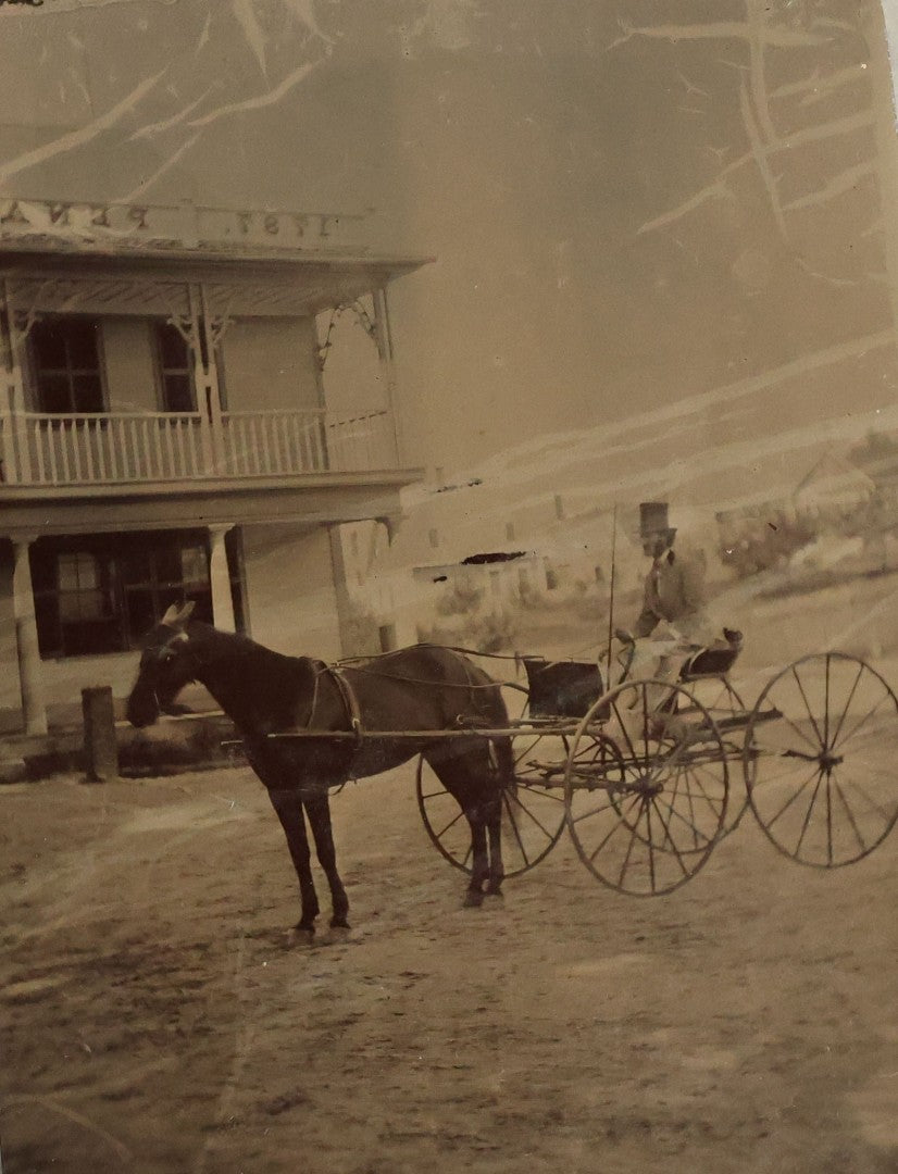 Lot 074 - Antique Outdoor Tintype Photograph Of Man In Stovepipe Hat Sitting On Horse Drawn Cart In Front Of A Building With Partial Sign Visible And Houses In Background