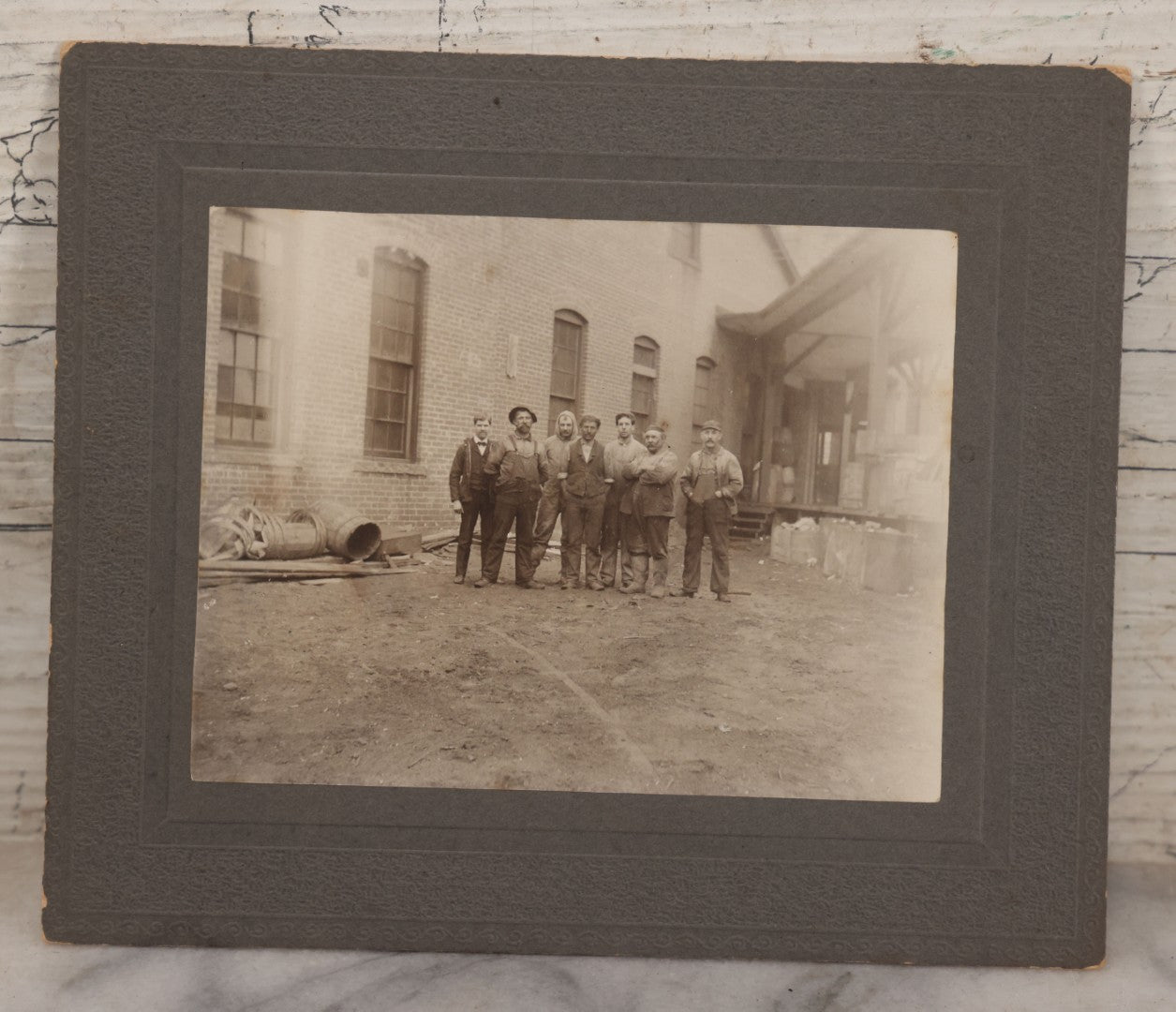 Lot 071 - Antique Boarded Occupational Photograph Of Group Of Seven Dirty Workers Posing In Work Clothes Outside Brick Workplace