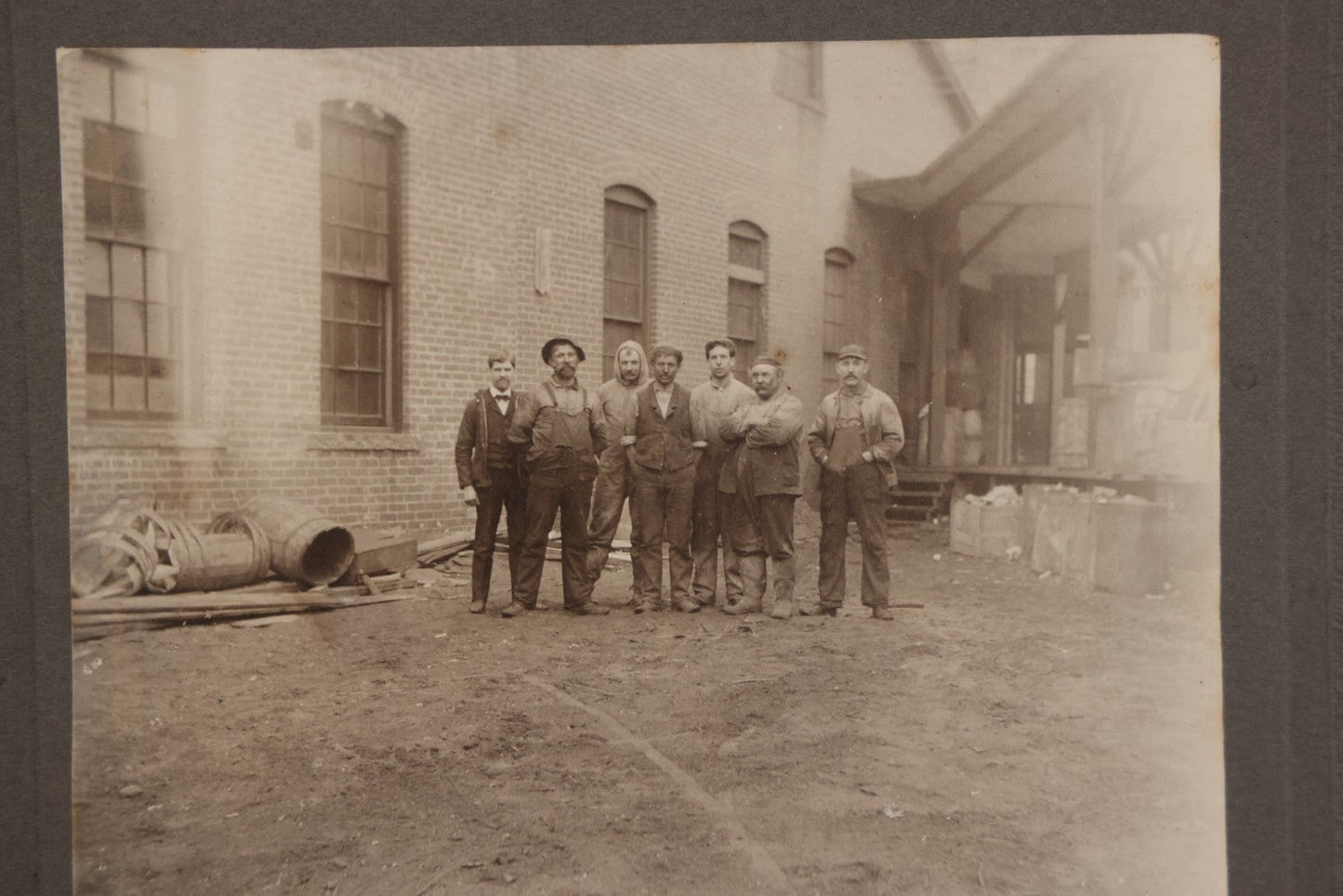 Lot 071 - Antique Boarded Occupational Photograph Of Group Of Seven Dirty Workers Posing In Work Clothes Outside Brick Workplace