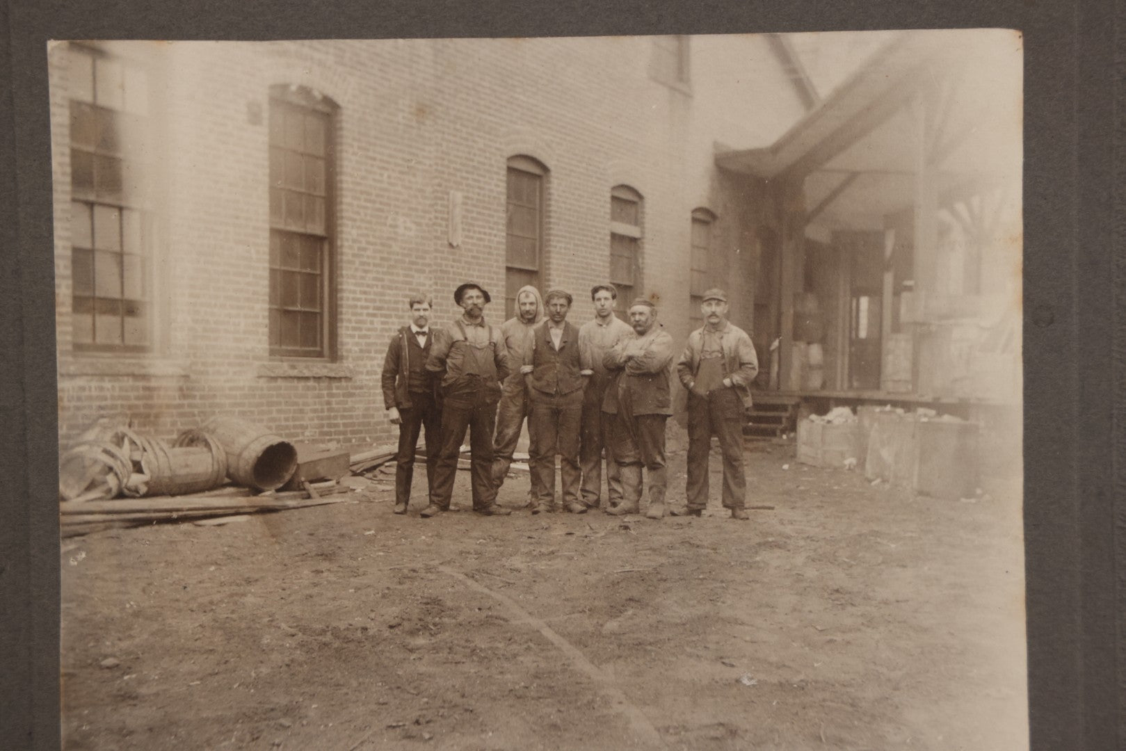 Lot 071 - Antique Boarded Occupational Photograph Of Group Of Seven Dirty Workers Posing In Work Clothes Outside Brick Workplace