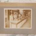 Lot 077 - Antique Boarded Occupational Photograph Of Two Butchers Behind Counter, With Sausage, Full Pig, And Other Meat Products Visible In Photo, And Large Commercial Scale