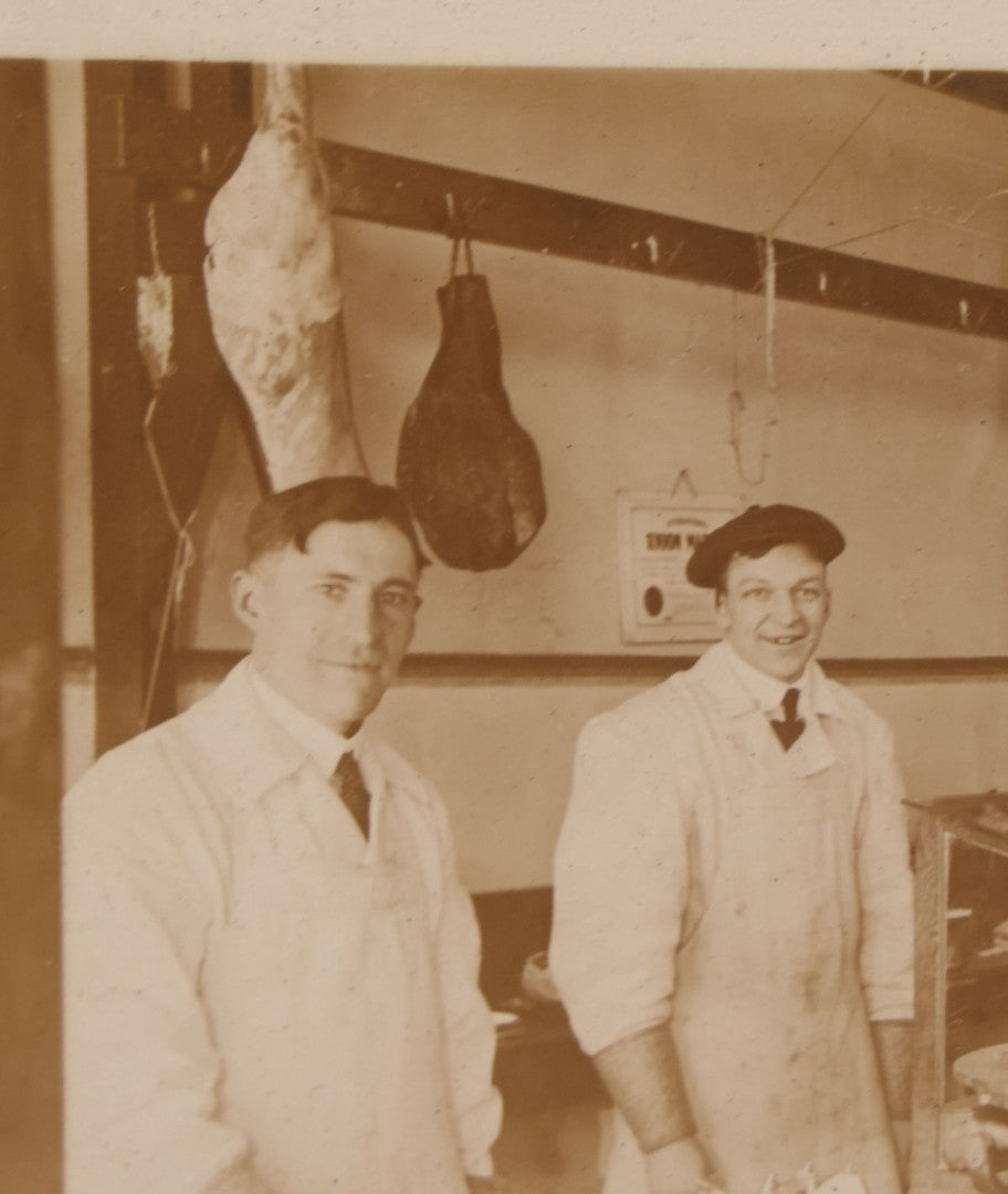 Lot 077 - Antique Boarded Occupational Photograph Of Two Butchers Behind Counter, With Sausage, Full Pig, And Other Meat Products Visible In Photo, And Large Commercial Scale