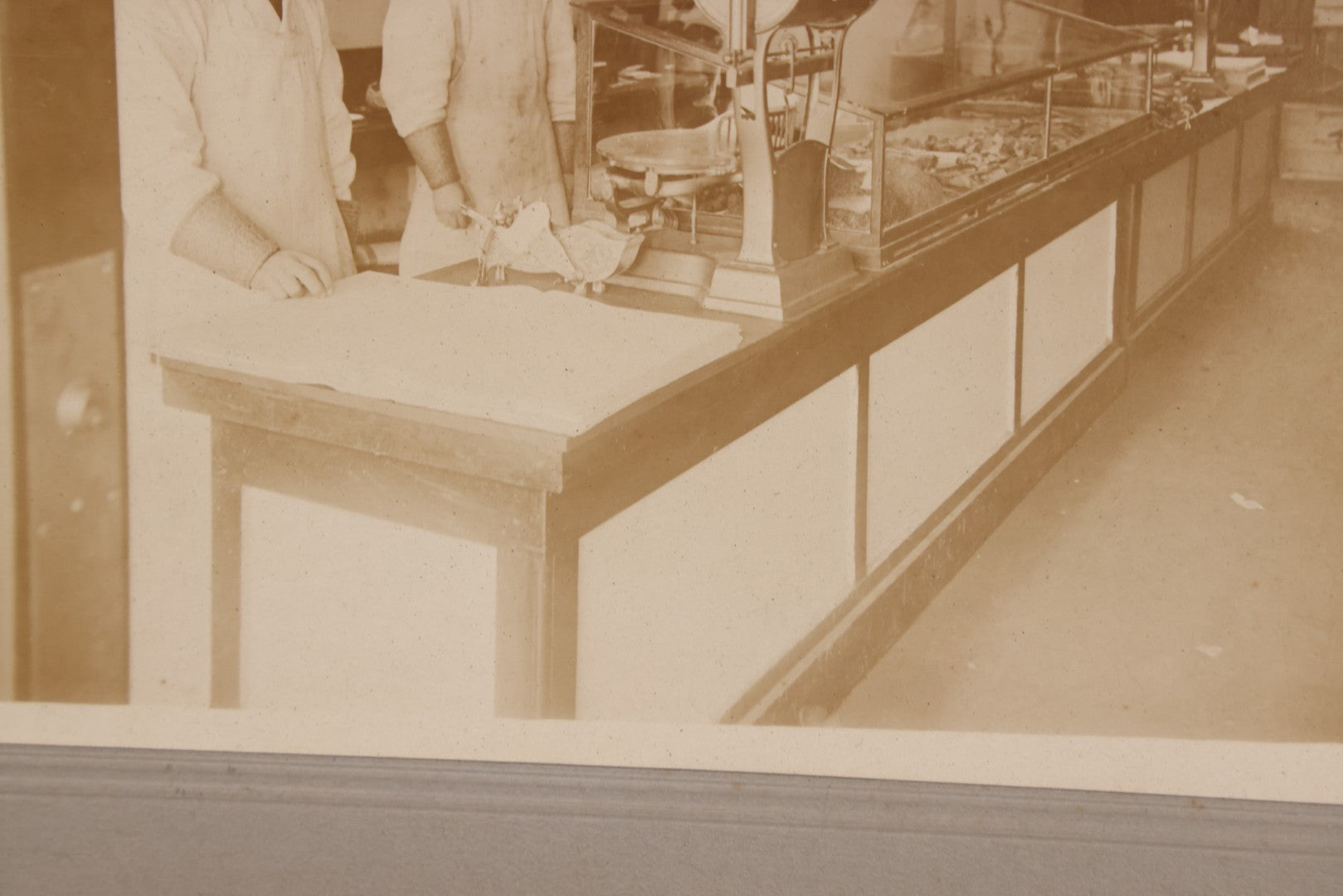 Lot 077 - Antique Boarded Occupational Photograph Of Two Butchers Behind Counter, With Sausage, Full Pig, And Other Meat Products Visible In Photo, And Large Commercial Scale