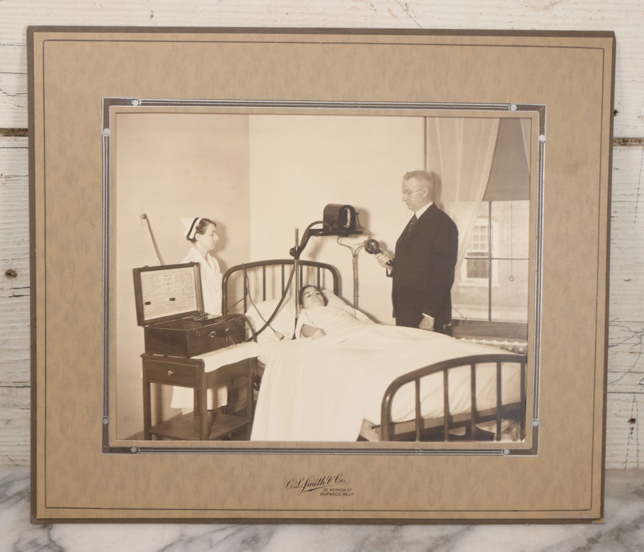 Lot 080 - Vintage Photograph In Paper Frame Of Woman In Hospital Bed With Her Nurse And Doctor About To Utilize An Unknown Medical Apperatus, C.L. Smith & Co., Photographers, Norwood, Massachusetts