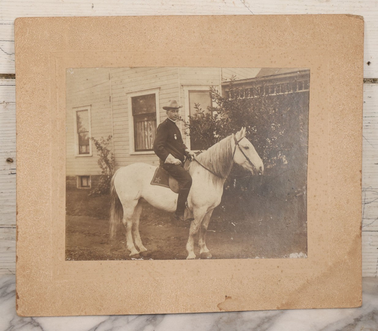 Lot 083 - Antique Boarded Photograph Of Man In Uniform Sitting Horseback On White Horse With Saddle Blanket Emblazoned With Star, Western Hat And Badge