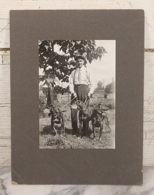Lot 090 - Vintage Boarded Photograph Of Man In High Waisted Pants With Suspenders Holding Three Hounds On Leashes