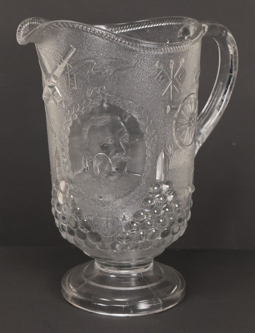 Lot 027 - Antique Early American Pattern Glass E.A.P.G. Spanish American War Battle Of Manila Bay Commemorative Pitcher With Admiral Dewey And U.S.S. Olympia, Patriotic Symbols Including Weaponry And Flags, Manufactured By Beatty-Brady Glass Co., Indiana