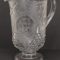 Lot 027 - Antique Early American Pattern Glass E.A.P.G. Spanish American War Battle Of Manila Bay Commemorative Pitcher With Admiral Dewey And U.S.S. Olympia, Patriotic Symbols Including Weaponry And Flags, Manufactured By Beatty-Brady Glass Co., Indiana