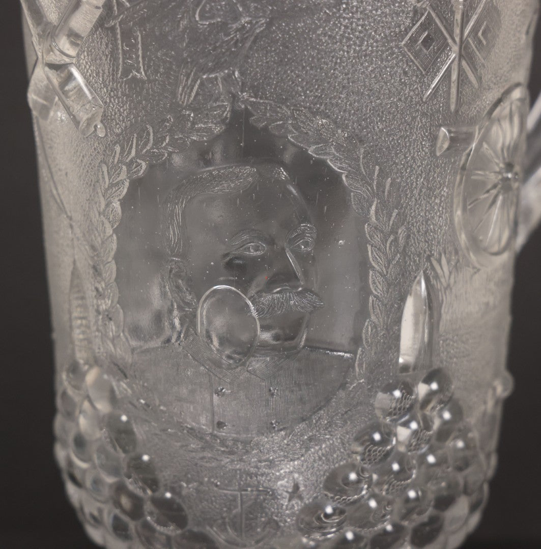 Lot 027 - Antique Early American Pattern Glass E.A.P.G. Spanish American War Battle Of Manila Bay Commemorative Pitcher With Admiral Dewey And U.S.S. Olympia, Patriotic Symbols Including Weaponry And Flags, Manufactured By Beatty-Brady Glass Co., Indiana
