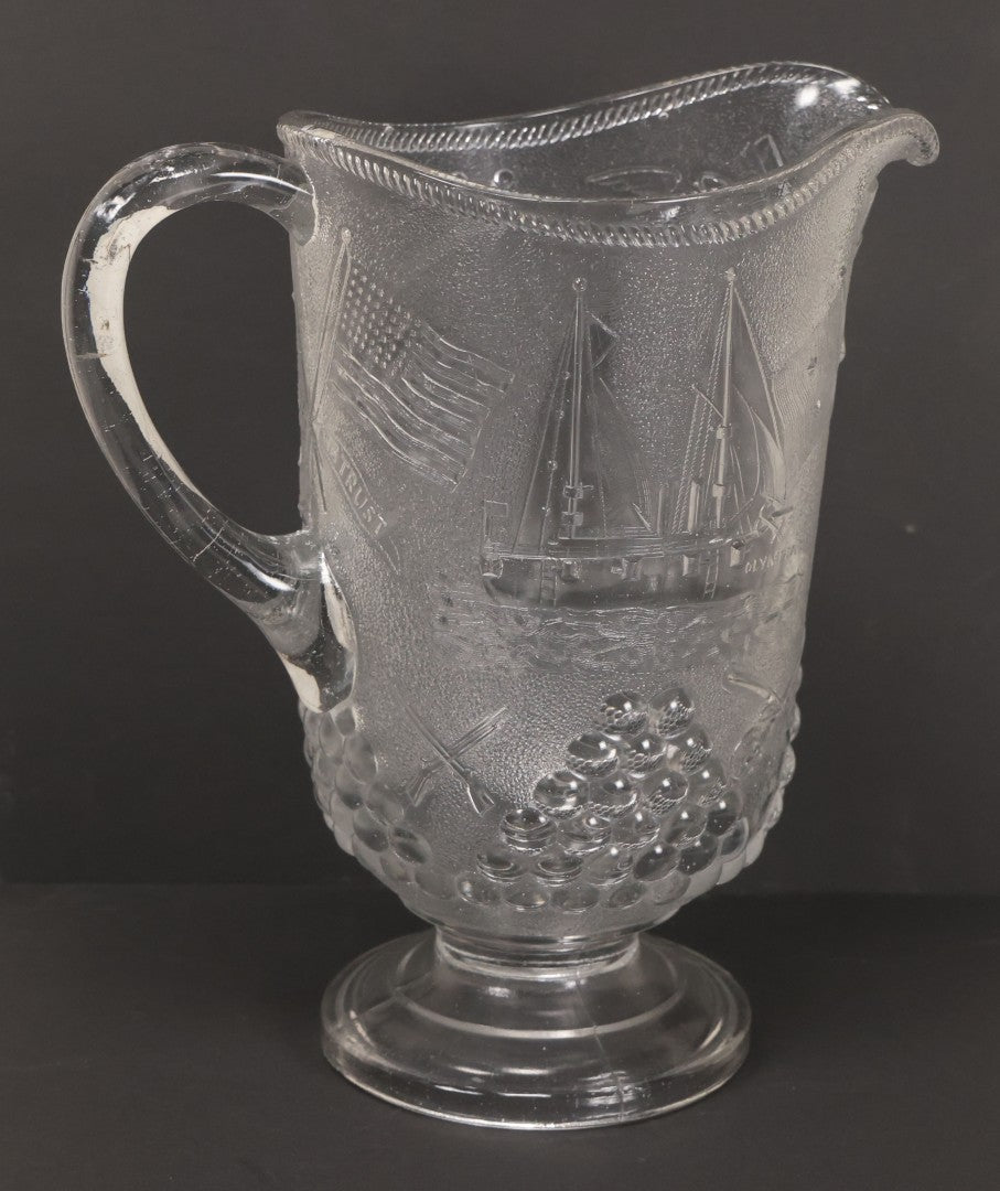 Lot 027 - Antique Early American Pattern Glass E.A.P.G. Spanish American War Battle Of Manila Bay Commemorative Pitcher With Admiral Dewey And U.S.S. Olympia, Patriotic Symbols Including Weaponry And Flags, Manufactured By Beatty-Brady Glass Co., Indiana