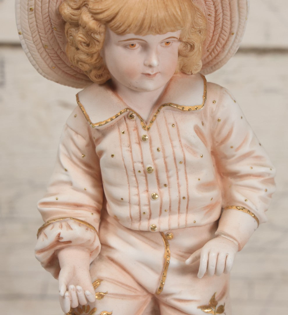Lot 037 - Vintage Bisque Statue Of Young Blond Child In Large Straw Hat Sitting By Shore With Pail, With Pink Painted Details And Gold Embellishments, Note Chip, Repairs, 12" Height