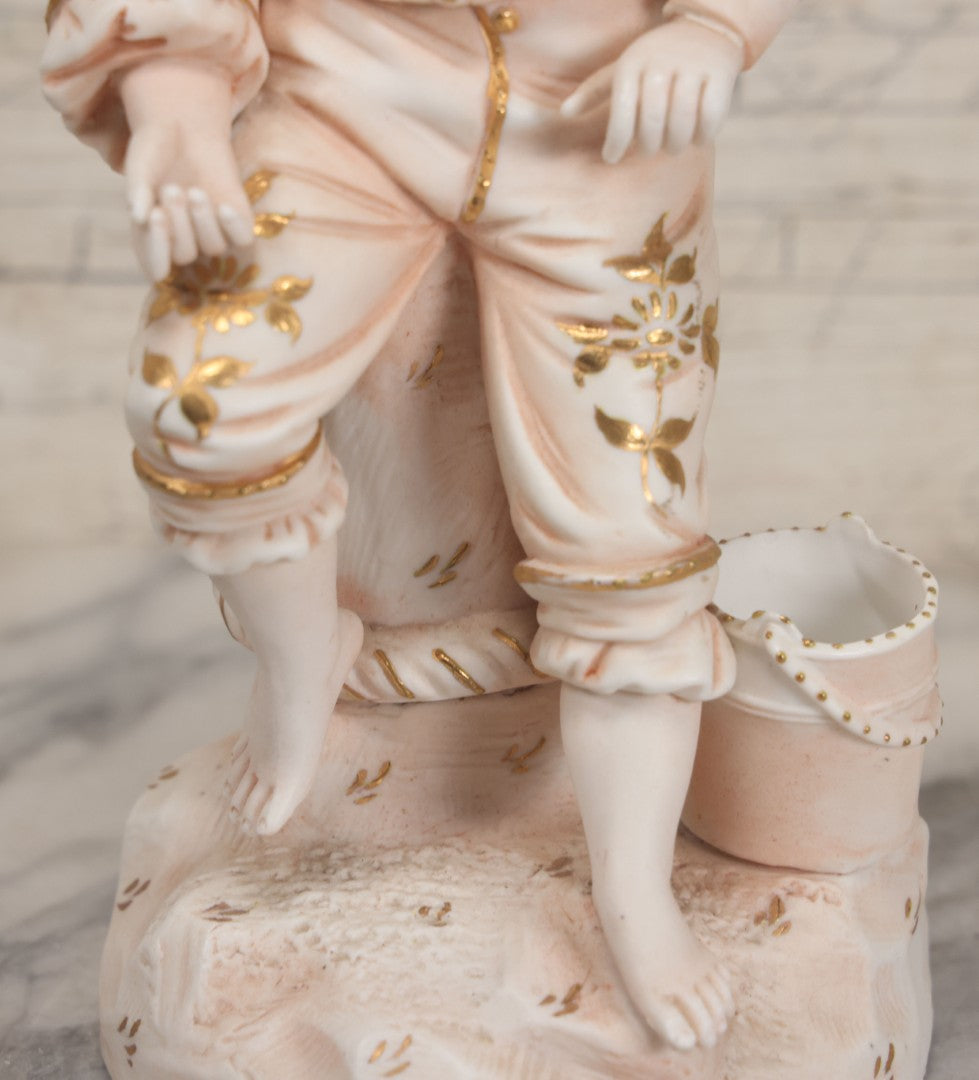Lot 037 - Vintage Bisque Statue Of Young Blond Child In Large Straw Hat Sitting By Shore With Pail, With Pink Painted Details And Gold Embellishments, Note Chip, Repairs, 12" Height