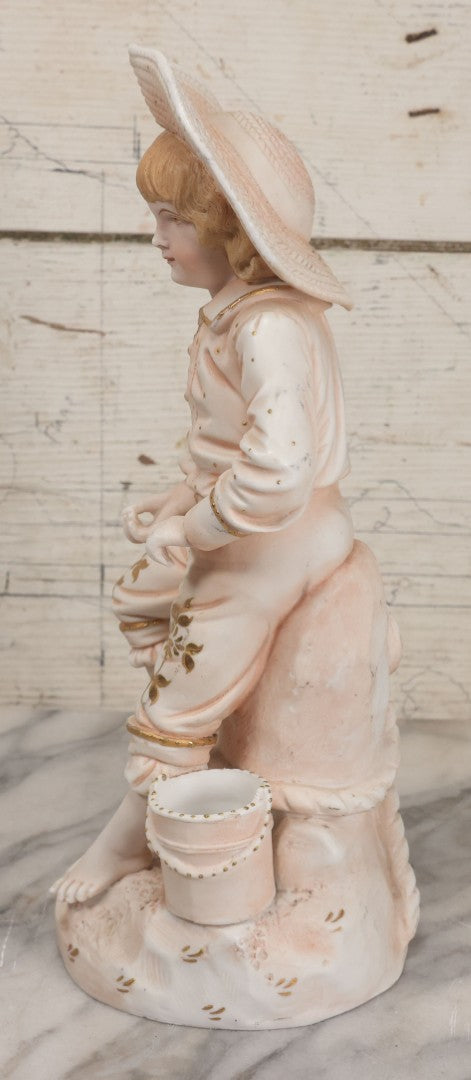 Lot 037 - Vintage Bisque Statue Of Young Blond Child In Large Straw Hat Sitting By Shore With Pail, With Pink Painted Details And Gold Embellishments, Note Chip, Repairs, 12" Height