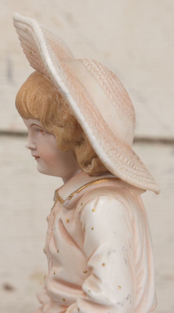 Lot 037 - Vintage Bisque Statue Of Young Blond Child In Large Straw Hat Sitting By Shore With Pail, With Pink Painted Details And Gold Embellishments, Note Chip, Repairs, 12" Height