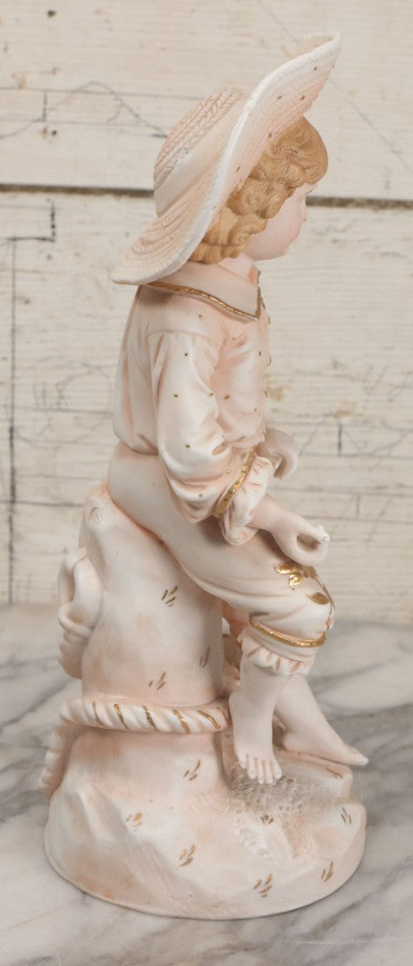 Lot 037 - Vintage Bisque Statue Of Young Blond Child In Large Straw Hat Sitting By Shore With Pail, With Pink Painted Details And Gold Embellishments, Note Chip, Repairs, 12" Height