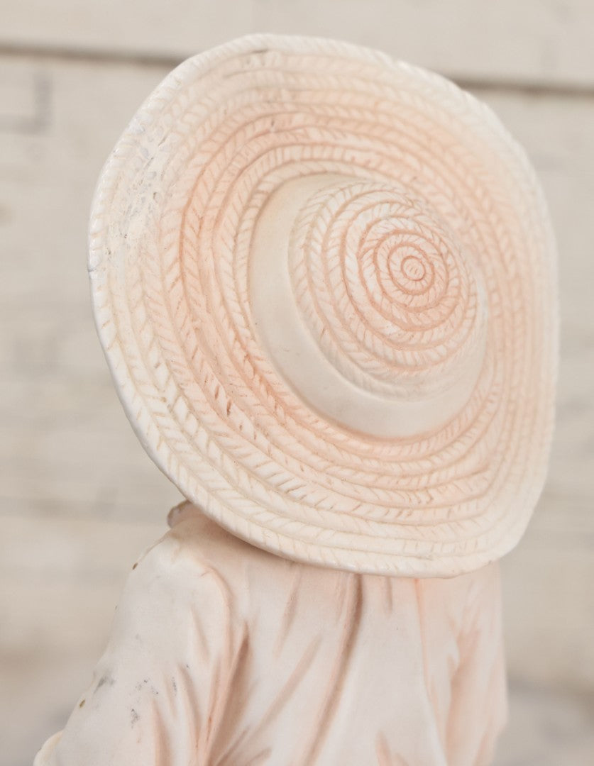 Lot 037 - Vintage Bisque Statue Of Young Blond Child In Large Straw Hat Sitting By Shore With Pail, With Pink Painted Details And Gold Embellishments, Note Chip, Repairs, 12" Height