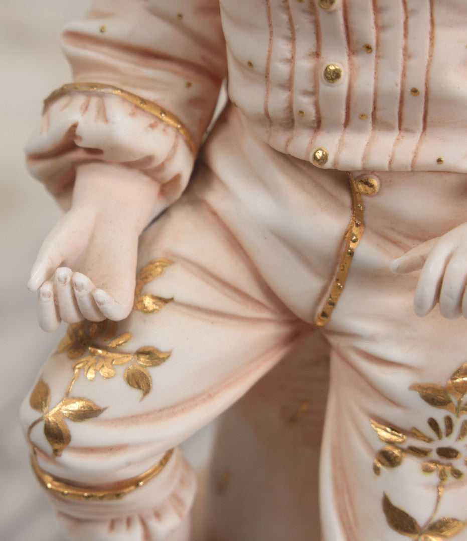 Lot 037 - Vintage Bisque Statue Of Young Blond Child In Large Straw Hat Sitting By Shore With Pail, With Pink Painted Details And Gold Embellishments, Note Chip, Repairs, 12" Height